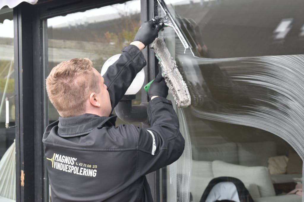 Professional cleaning service washing a large glass window. Clean and efficient work by a dedicated individual.